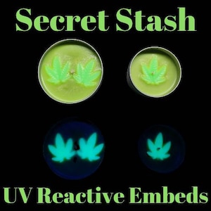Puede incluir: Dos velas verdes con un diseño de hoja que brillan bajo una luz negra. Las velas están etiquetadas como "Secret Stash" y "UV Reactive Embeds".