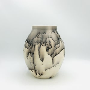 May include: A ceramic vase with a rounded body and a wide opening. The vase features a cream-colored base with a gray and black pattern that resembles a topographical map. The rim is a solid gray color.