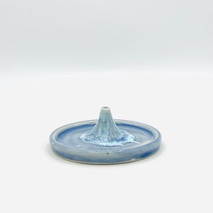 May include: A ceramic ring holder in the shape of a mountain. The ring holder is light blue with a white and light blue mountain peak in the center. The base is a shallow dish.
