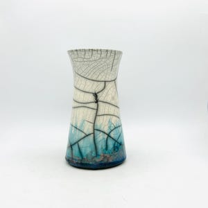 May include: A ceramic vase with a unique crackle glaze. The vase transitions from a white top to a turquoise and blue base. The vase has a flared top and a slightly wider base, standing approximately 6 inches tall.