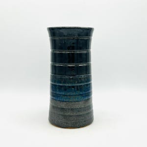 May include: A dark blue and gray ceramic vase with a textured, striped design. The vase is tall and slender, with a rounded base.
