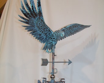 Puede incluir: Una veleta de cobre con un águila detallada con las alas extendidas. El águila está posada sobre una flecha direccional y una rosa de los vientos con los puntos cardinales. El metal tiene una pátina azul-verdosa.