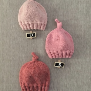 May include: Three knitted hats with a knot on top. The hats are pink and red. The hats are labelled with letters D, E, and F.