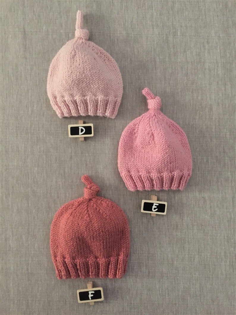 May include: Three knitted hats with a knot on top. The hats are pink and red. The hats are labelled with letters D, E, and F.
