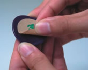 May include: A purple round adhesive bandage with a green adhesive backing. The bandage is being peeled off of a purple round backing.