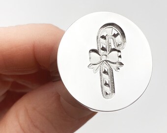 May include: A silver metal stamp with a design of a candy cane with a bow on top.