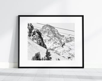Puede incluir: Una fotografía en blanco y negro de una cordillera nevada con una persona montando un telesilla. La persona está sentada en una silla y mirando el paisaje. La cordillera está cubierta de nieve y hay árboles en primer plano.