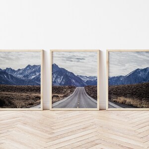 May include: Three framed landscape photographs of a mountain range with a road leading through the center of the image. The mountains are a dark blue color and the road is a light gray color.