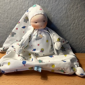 Pu&ograve; includere: Una bambola di stoffa bianca con un cappello di stoffa bianca, che indossa un pigiama bianco e blu a fantasia con un piccolo disegno di topo. La bambola &egrave; seduta su una coperta bianca e blu a fantasia con un piccolo disegno di topo.