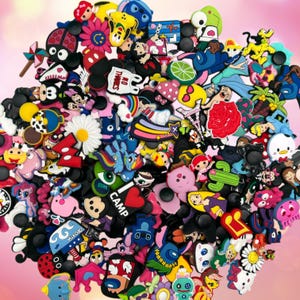 May include: A collection of colorful shoe charms in various shapes and designs. The charms feature cartoon characters, flowers, and other decorative elements. The charms are made of rubber and have a black backing for attachment to shoes.