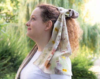 May include: A woman with curly red hair wears a white t-shirt and green pants. She has a floral patterned scarf tied around her hair.