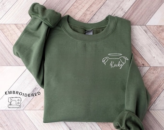 May include: Olive green sweatshirt with embroidered dog design and the name "Rocky" in white. The sweatshirt has a crew neck and long sleeves with ribbed cuffs. The word "EMBROIDERED" is printed on the left side of the image.