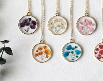 May include: Six gold necklaces with round pendants featuring pressed flowers. The pendants are clear and show different colored flowers, including purple, white, pink, orange, blue, and red.