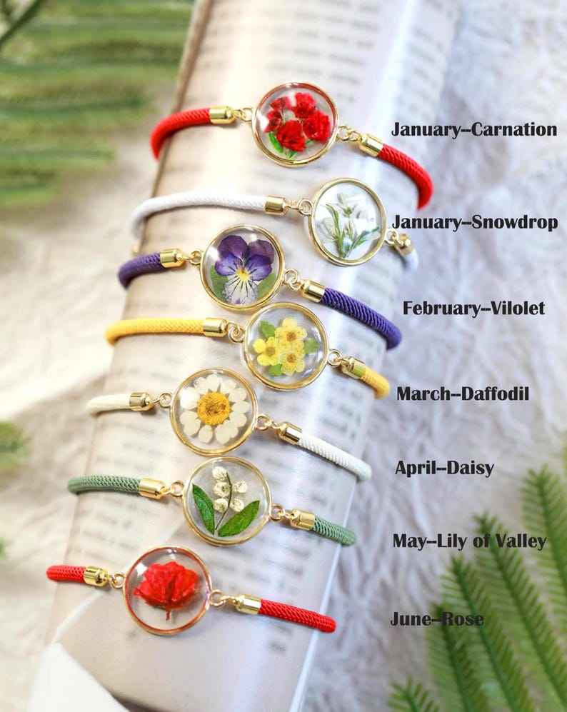 May include: A collection of bracelets featuring pressed flowers encased in clear resin. Each bracelet has a different flower, including carnation, snowdrop, violet, daffodil, daisy, lily of the valley, and rose. The bracelets are labeled with the month and flower name.