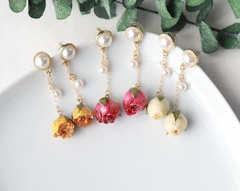 May include: Six pairs of gold earrings with pearl accents and dried flower charms. The flowers are pink, yellow, and white.