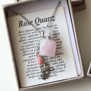 May include: A rose quartz necklace with a small pink stone bottle pendant, a pink tassel, and a silver charm. The necklace is displayed in a gray box with text that reads "Rose Quartz".