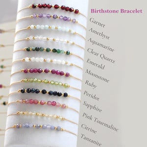 May include: A collection of delicate birthstone bracelets. Each bracelet features a string of small, colorful gemstones, including garnet, amethyst, and emerald, with gold-colored accents. The text "Birthstone Bracelet" is displayed in the upper right corner.