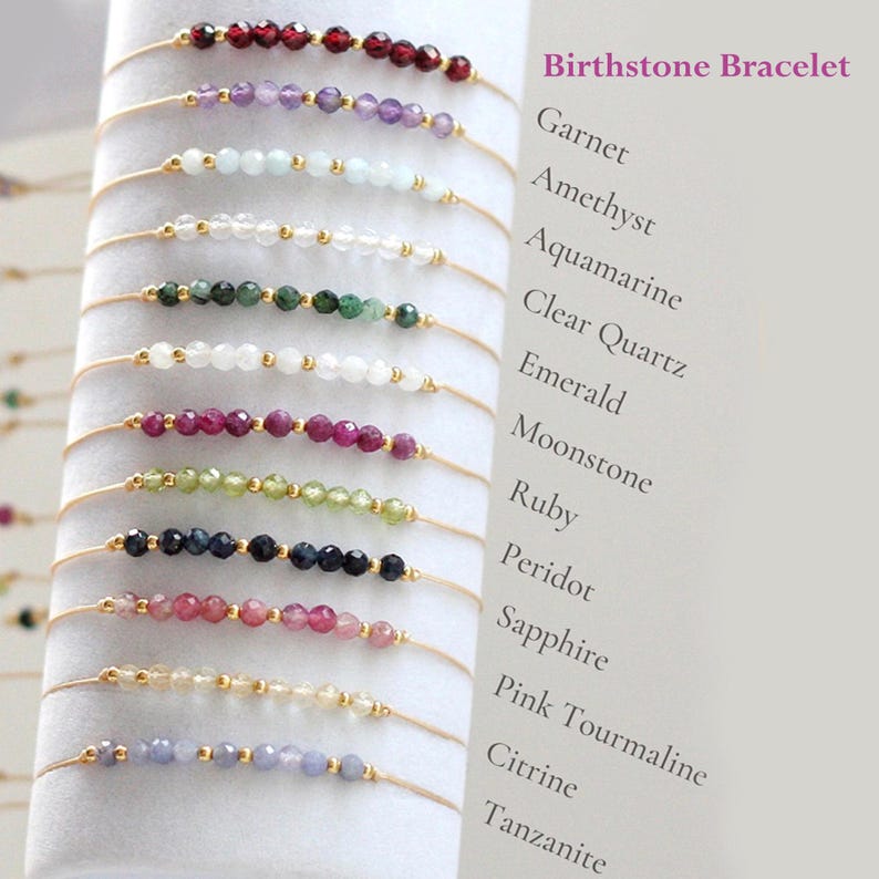 May include: A collection of delicate birthstone bracelets. Each bracelet features a string of small, colorful gemstones, including garnet, amethyst, and emerald, with gold-colored accents. The text "Birthstone Bracelet" is displayed in the upper right corner.