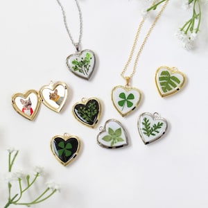 May include: A set of nine gold heart-shaped locket necklaces with different pressed flower and leaf designs. Some lockets feature a single leaf, while others have multiple leaves or flowers. The lockets are all on delicate gold chains.
