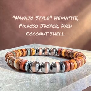 May include: A beaded bracelet featuring metallic hematite spheres, round Picasso jasper beads, and flat dyed coconut shell discs. The text "NAVAJO STYLE" HEMATITE, PICASSO JASPER, DYED COCONUT SHELL is displayed above the bracelet in a light font.
