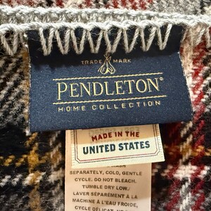 May include: A Pendleton Home Collection blanket label featuring a dark blue tag with gold text and a teepee logo. Below it, a smaller white tag reads Made in the United States, followed by care instructions in English and French on a long fabric strip.