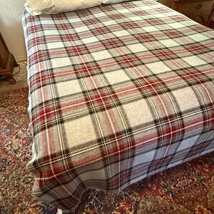 May include: A bed blanket featuring a classic plaid pattern in shades of light gray, deep red, and black. The woven fabric displays a repeating grid design that covers the entire surface of the bed, providing a textured appearance across the bedding.