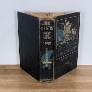 May include: A vintage book titled "Our Country" from 1935, with a black cover and gold lettering. The spine displays "West and West" and a nautical illustration. The book's cover features a sailing ship illustration.