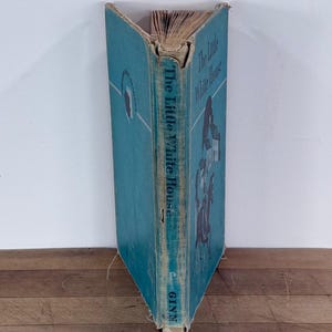 May include: A vintage hardcover book titled The Little White House published by Ginn. The book features a teal blue cover with dark blue text and a graphic illustration of a house and a person on a horse. The spine shows signs of wear and age.