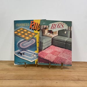 May include: Two vintage crochet rug pattern books. One book has a teal cover with the title "Crocheted Rugs" and illustrations of rugs. The other book has a green cover with the title "Rugs" and a pink rug illustration.