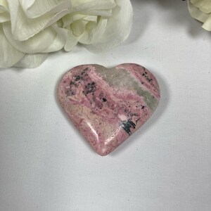May include: A heart-shaped pink and gray stone with black veins. The stone is polished and smooth.
