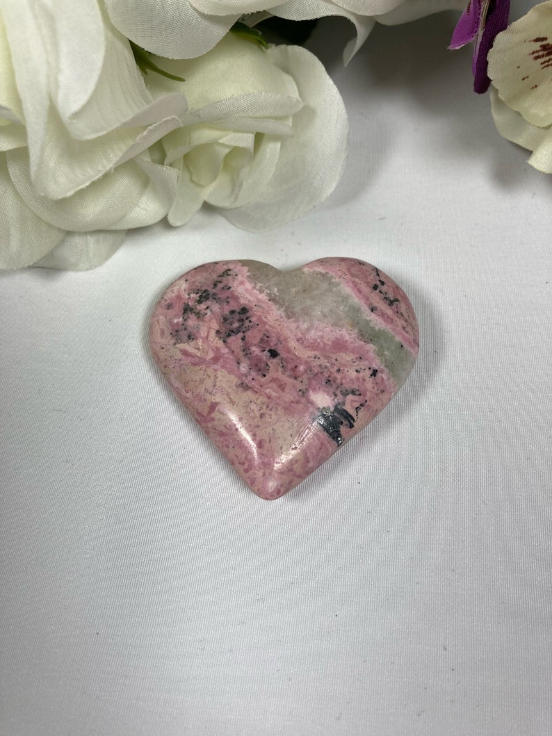 May include: A heart-shaped pink and gray stone with black veins. The stone is polished and smooth.