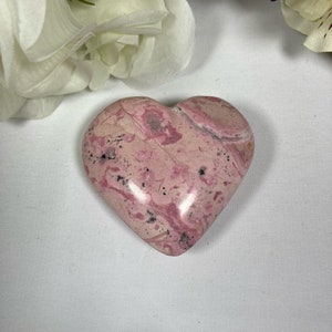 May include: A pink and white heart-shaped stone with a marbled pattern. The stone is smooth and polished.