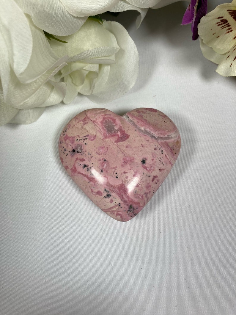 May include: A pink and white heart-shaped stone with a marbled pattern. The stone is smooth and polished.