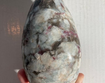 May include: A polished, egg-shaped crystal with a swirling pattern of white, gray, and pink.