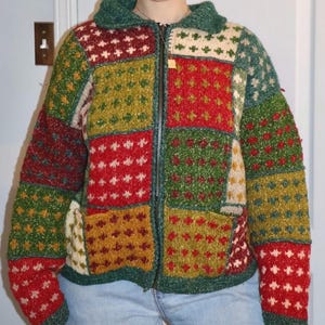 May include: A colourful patchwork zip-up cardigan. The design incorporates squares of red, green, yellow, and cream, with dotted and star patterns. It has a collared neckline and two front pockets. The garment is a cozy, knitted style.