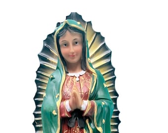 May include: A figurine of the Virgin Mary, Our Lady of Guadalupe, in a green and red robe with a gold trim. She is standing on a crescent moon with her hands clasped in prayer. The figurine is surrounded by a golden halo.