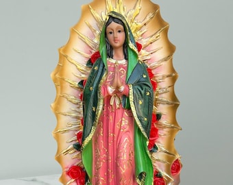 May include: A detailed statue of the Virgin Mary, featuring a pink and gold dress, green shawl, and a golden halo. Red roses and a small figure adorn the base. The statue is a religious item.