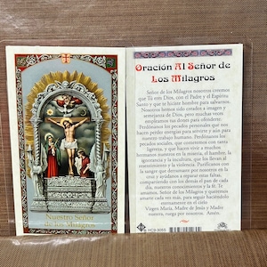 May include: A religious prayer card featuring an image of Jesus on the cross, with two figures on either side. The card has text in Spanish, including "Nuestro Señor de los Milagros" and "Oración Al Señor de Los Milagros."