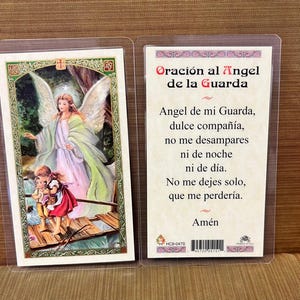 May include: A laminated prayer card featuring an illustration of a guardian angel watching over two children on a wooden bridge. The reverse side displays the text Oración al Angel de la Guarda, followed by a Spanish prayer and a barcode.