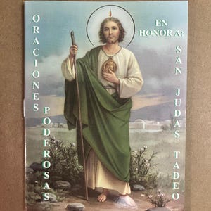 May include: A religious print featuring a saintly figure in a white robe and green cloak, holding a staff. The image includes text in Spanish: "ORACIONES PODEROSAS EN HONOR A SAN JUDAS TADEO."