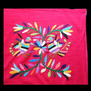 May include: A vibrant pink fabric with colorful embroidered birds and flowers. The birds are facing each other and are surrounded by green leaves and flowers in shades of blue, yellow, orange, and purple.