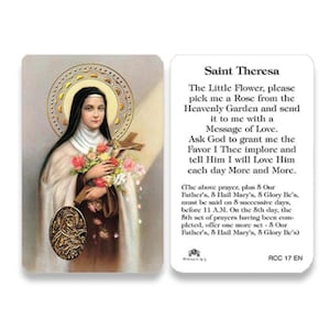 May include: A prayer card featuring Saint Theresa, holding a crucifix and flowers, with a halo. The card includes a prayer text and the text "Saint Theresa". The card has a gold medallion and is set against a white background.