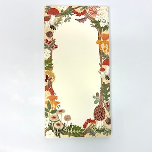 May include: A cream-colored card with a border of colorful mushrooms, flowers, and leaves. The border is arranged in a circular pattern around a blank space in the center.