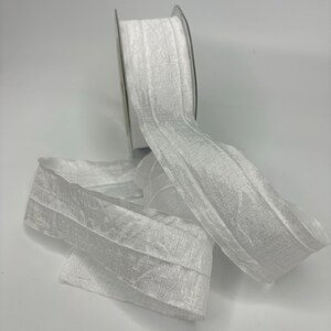 May include: White crinkled ribbon with a textured surface. The ribbon is rolled up on a spool.