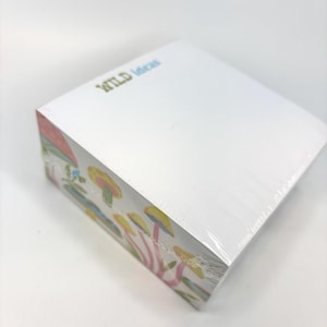 May include: A white notepad with the words "WILD Ideas" in green and blue. The side of the notepad features a colorful illustration of mushrooms in yellow, pink, and blue.