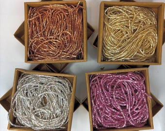 May include: Four small, square, open-top boxes filled with metallic, coiled strands. The colors are copper, gold, silver, and magenta. The boxes are made of light brown cardboard and are arranged on a white surface.