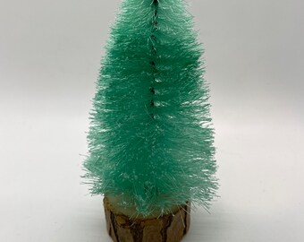 May include: A small, green, bottle brush Christmas tree with a brown wooden base.