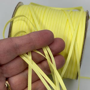 May include: A spool of bright yellow satin ribbon. The ribbon is thin and has a subtle sheen.