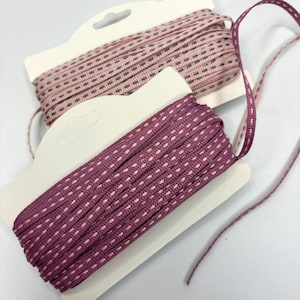 May include: Two spools of pink and purple ribbon with a dotted pattern. The ribbon is on a white card with a hanging hole.