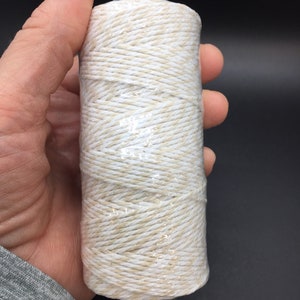 May include: A tightly wound roll of natural twine, wrapped in clear plastic. The twine is a mix of white and beige fibers, creating a textured appearance. Ideal for crafting, gift wrapping, or general household use.